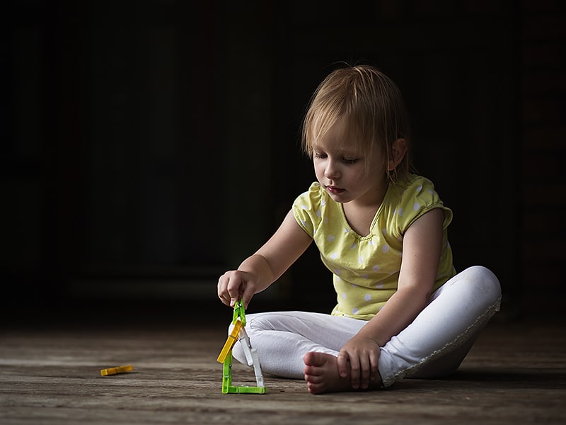 I was fascinated by the beautiful light on my porch before a storm. I laid a few clothespins on the porch for my daughter in the spot where I wanted to photograph her. Right away she started turning them into a house. Canon EOS 6D, Canon EF 85/1.8, 1/400 s, f/2.2, ISO 100, focal length 85 mm