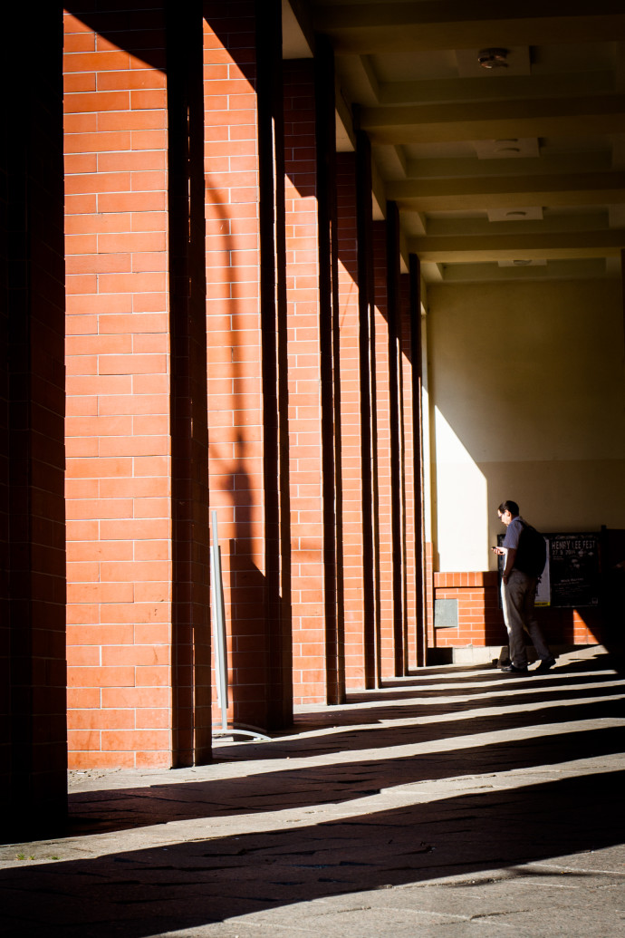 The reddened columns are separated, via their colors, from the grayish stripes of light breaking through onto the sidewalk. The yellow on the roof—even though it’s in shadow—is still visible enough to draw attention to itself, just like the man’s blue shirt. 