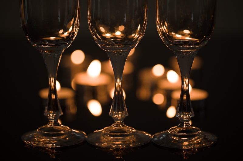 Three glasses side-by-side. Their shapes are only visible because the candlelight from the background is refracted in them. Canon 5D Mark IV, Canon EF 100/2.8 IS MACRO, 1/50 s, f/2.8, ISO 200, focal length 100 mm