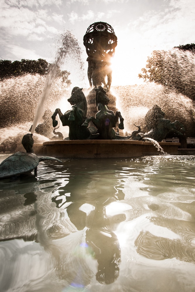 A fountain along with its reflection in the water.