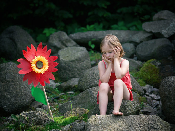 Photographing Kids in Colors and Black and White: a synthetic flower and a child sitting on stones.